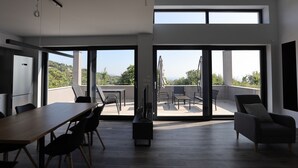 Una habitación amplia con una mesa grande y sillas, un televisor de pantalla plana y un balcón con mobiliario exterior.