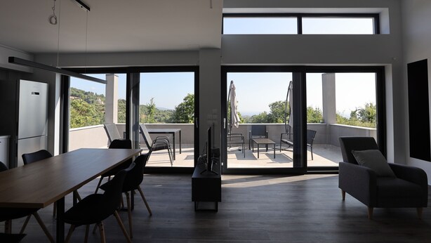 Una habitación amplia con una mesa grande y sillas, un televisor de pantalla plana y un balcón con mobiliario exterior.