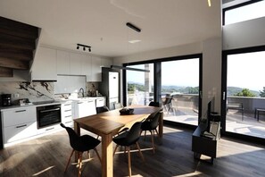 Une cuisine moderne avec des meubles blancs, une table à manger en bois et une vue sur l’extérieur.