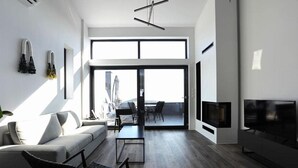 Un salon moderne comprenant un canapé, une table basse, un téléviseur et un balcon aménagé avec du mobilier d’extérieur.