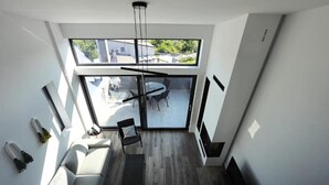 Un interior moderno con un sofá, una mesa de comedor y sillas, una lámpara de techo y un ventanal con vistas al exterior.