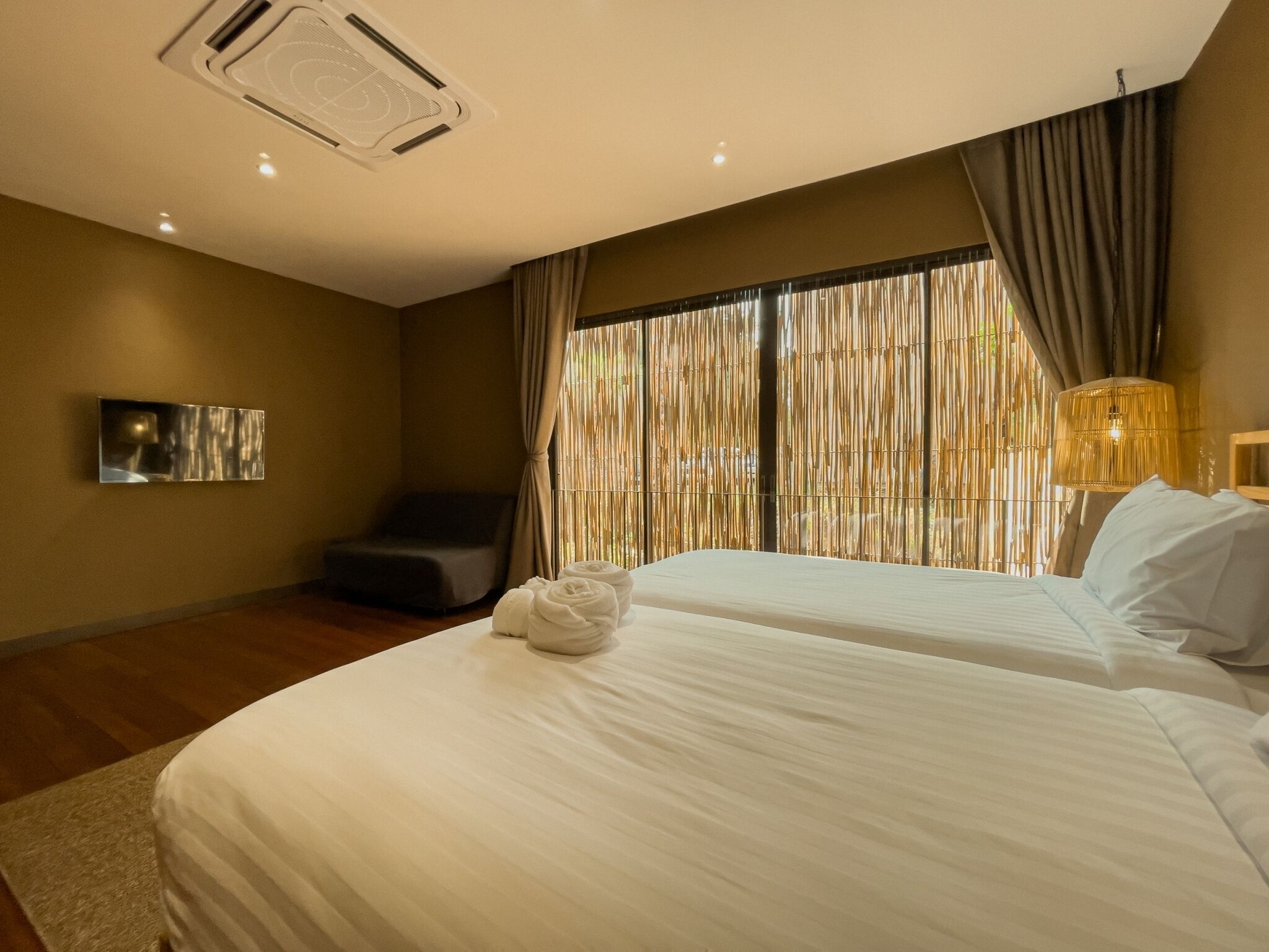 A hotel room with two beds, a seating area, a wall-mounted TV, and a large window with curtains.