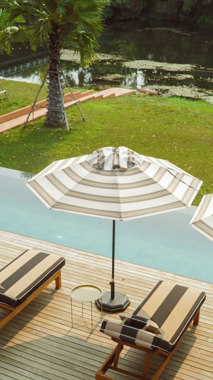 Uma área de piscina com espreguiçadeiras e um guarda-sol listrado.
