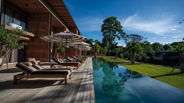 Un resort moderno con terraza de madera, sillones de descanso y piscina.
