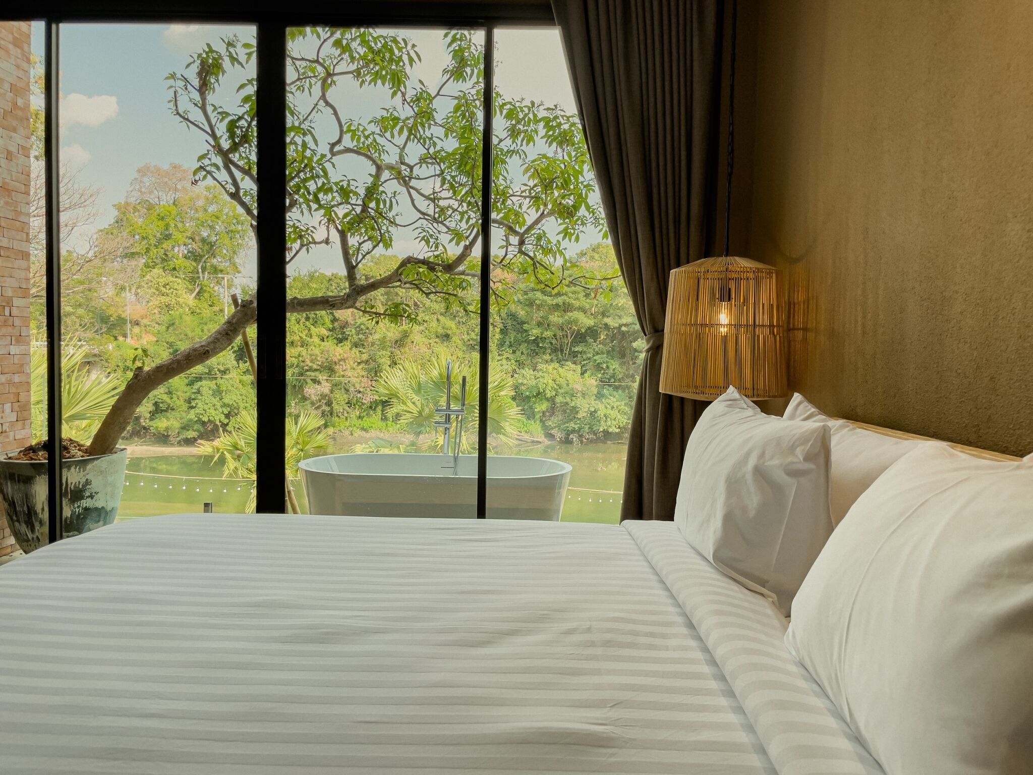 A hotel room with a large bed, a view of a lake, and a bamboo lamp.