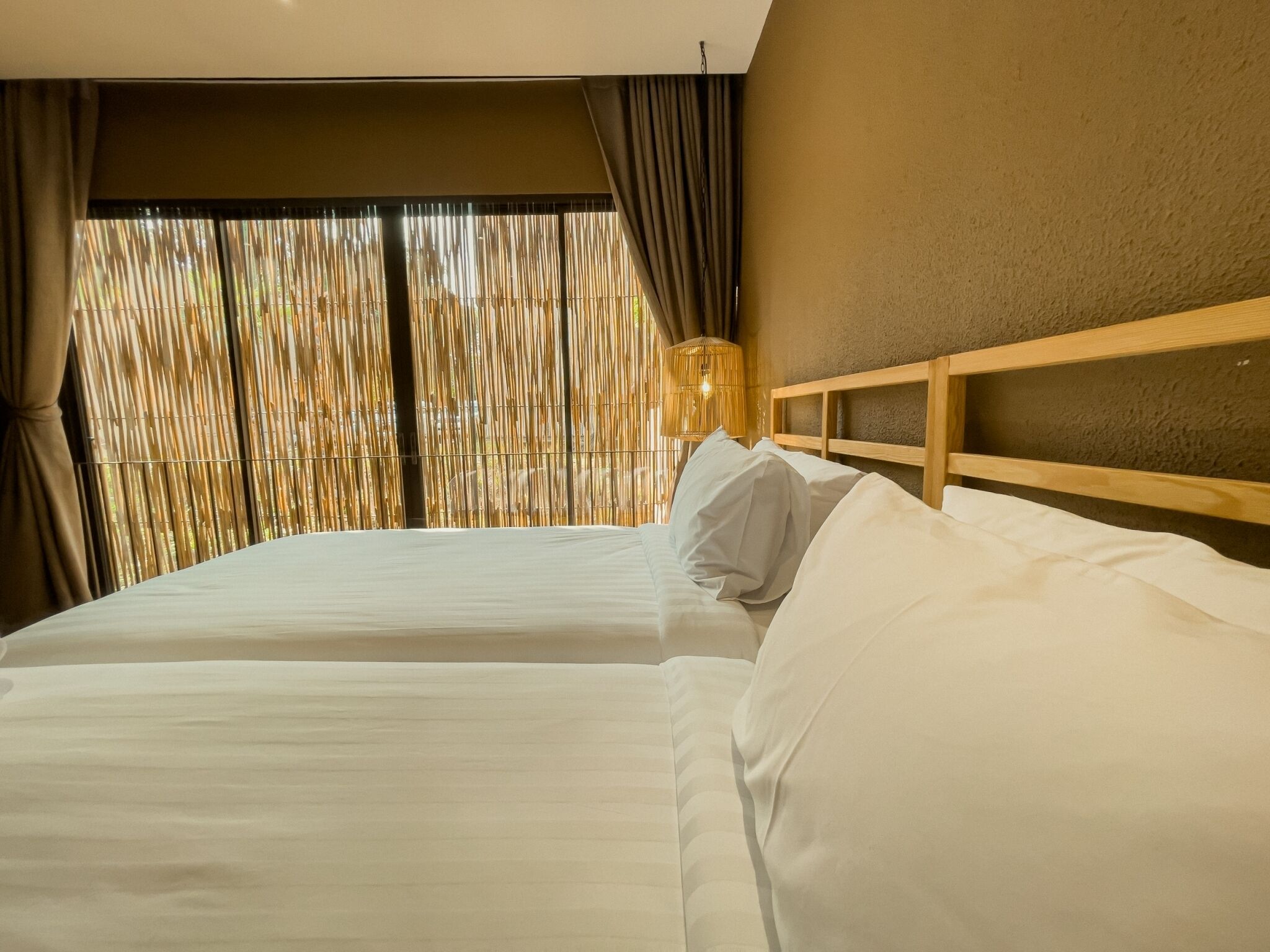Habitación de hotel con dos camas, un ventanal con cortinas y un cabecero de madera.