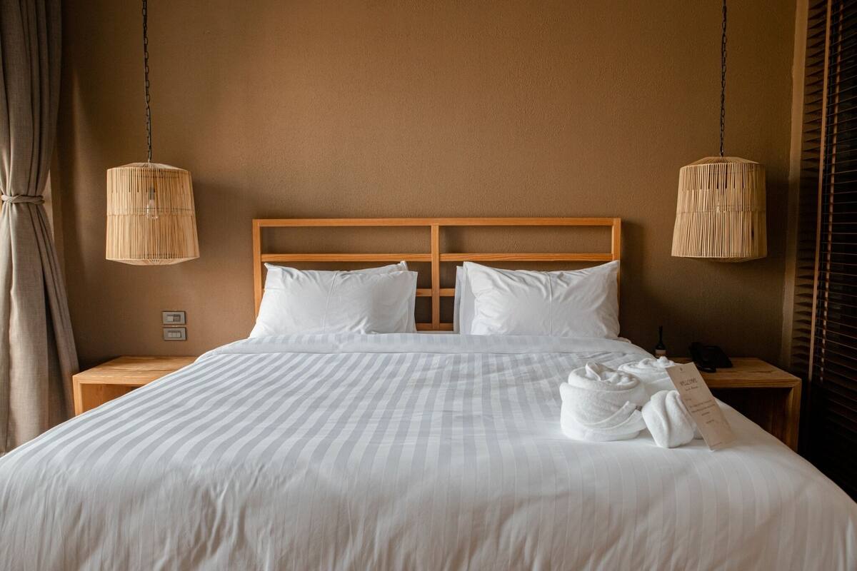 A neatly made bed with white linens, two bedside tables, and two hanging wicker lamps.