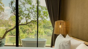 Un dormitorio con una cama grande, vistas a un estanque y un árbol fuera de la ventana.