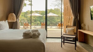 Habitación de hotel con una cama grande, un escritorio y vistas a un patio exterior con sombrillas y sillas.