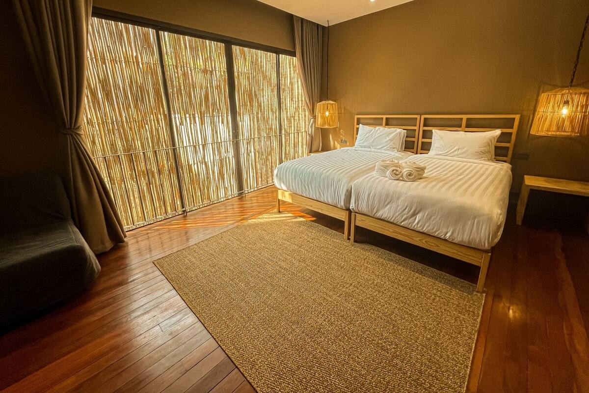 A modern bedroom with a large bed, wooden floor, and a view through a bamboo curtain.