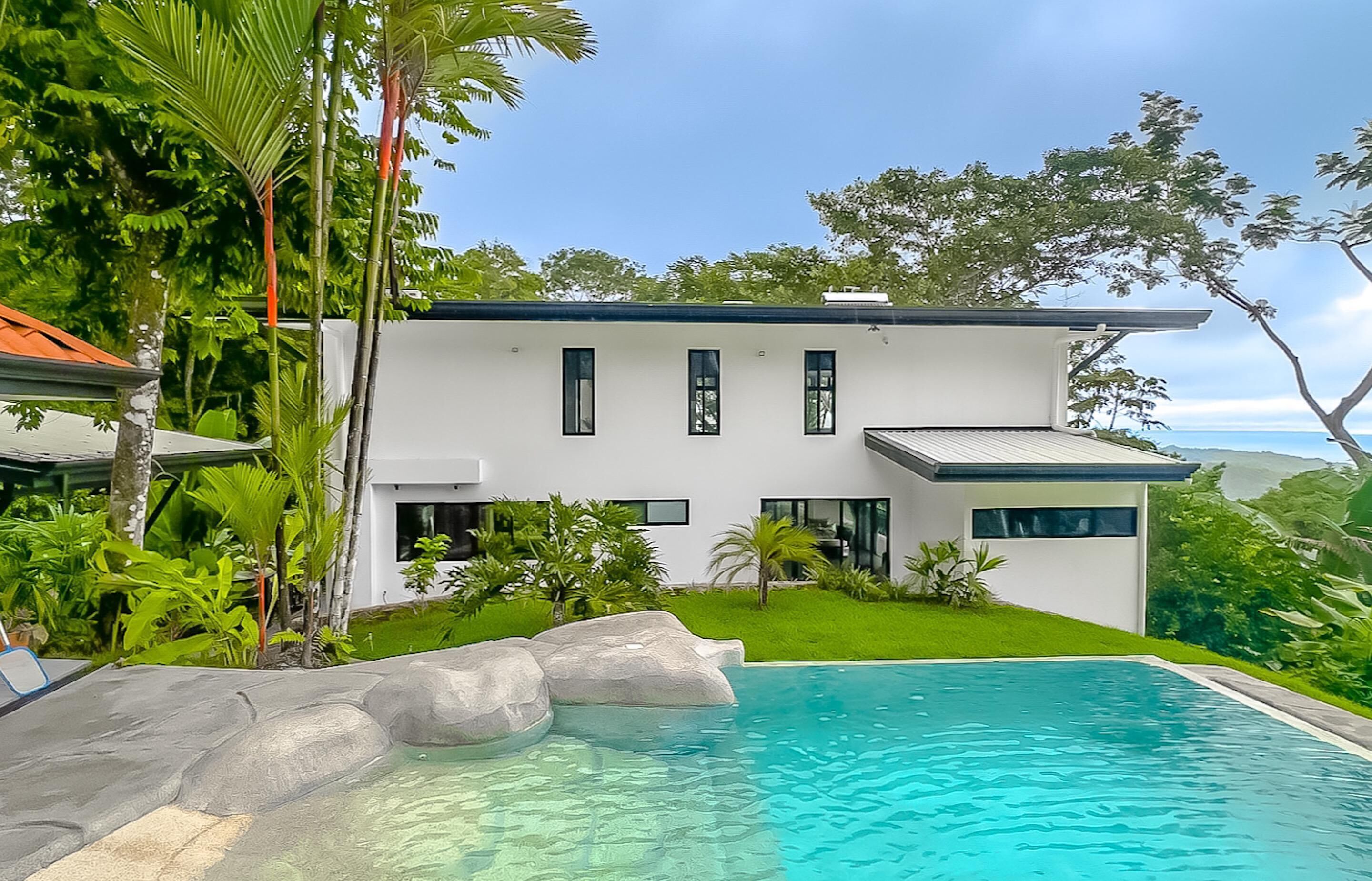 A modern two-story house with a swimming pool, surrounded by lush greenery and a clear sky.