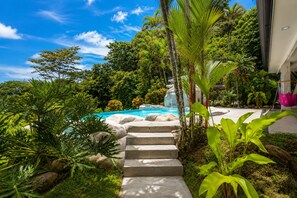 Une piscine avec des marches menant à l’eau, entourée d’une végétation tropicale et sous un ciel dégagé.