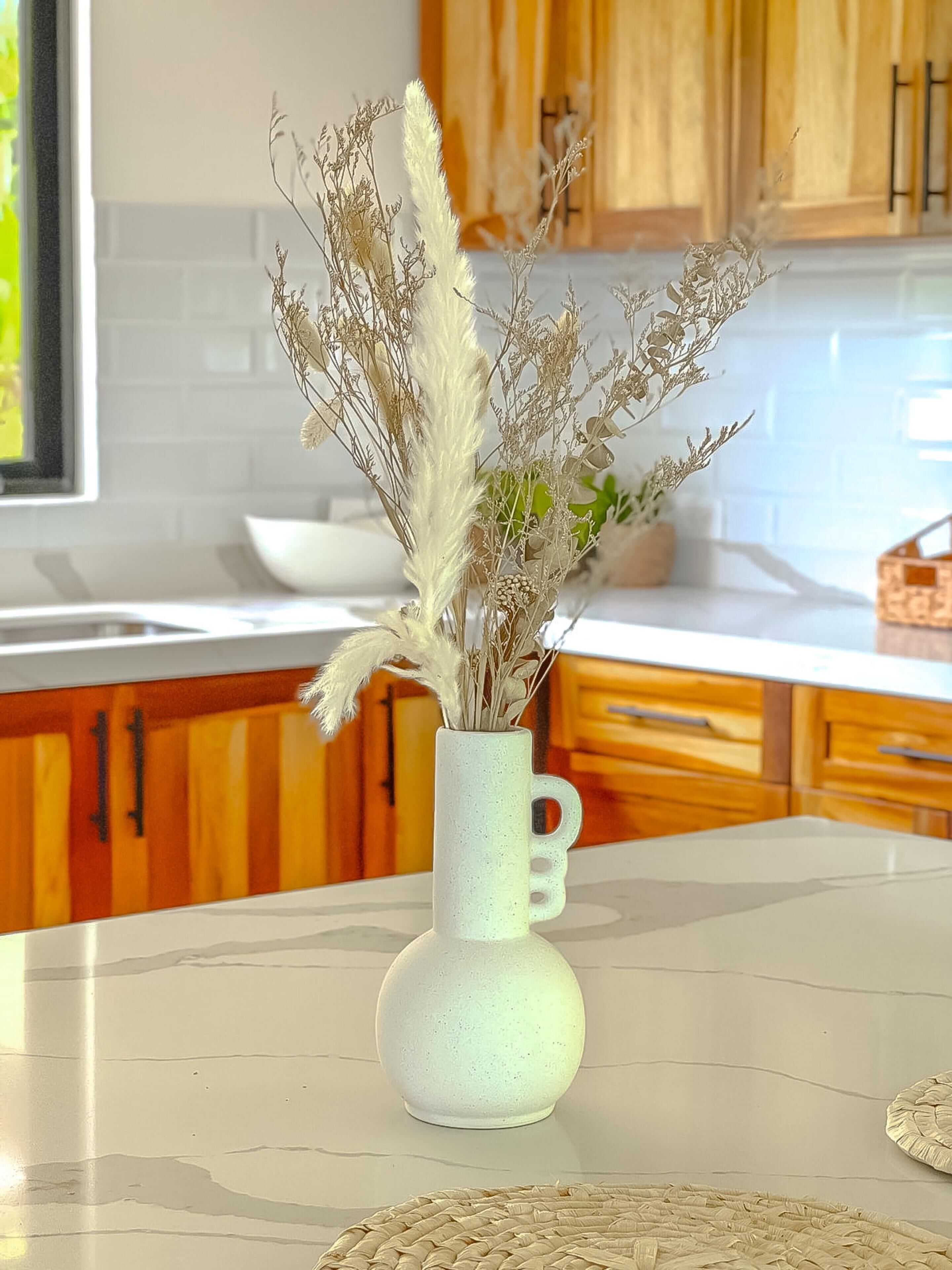 Cozinha com armários de madeira, bancada branca e um vaso com plantas secas.