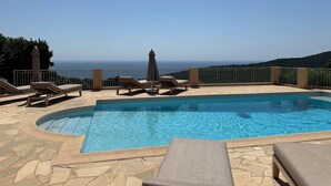 Un espace piscine doté de chaises longues et d’un parasol, offrant une vue panoramique sur la mer.