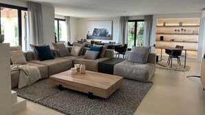 Un salon moderne avec un canapé d’angle, une table basse en bois et un coin repas comprenant une table et des chaises.