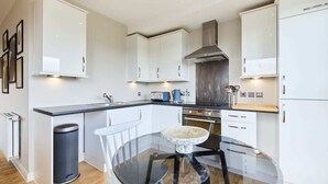 A modern kitchen with white cabinets, a stainless steel range hood, and a glass dining table. - The Enfield Sanctuary - Modern 1bdr Flat With Balcony (Enfield)