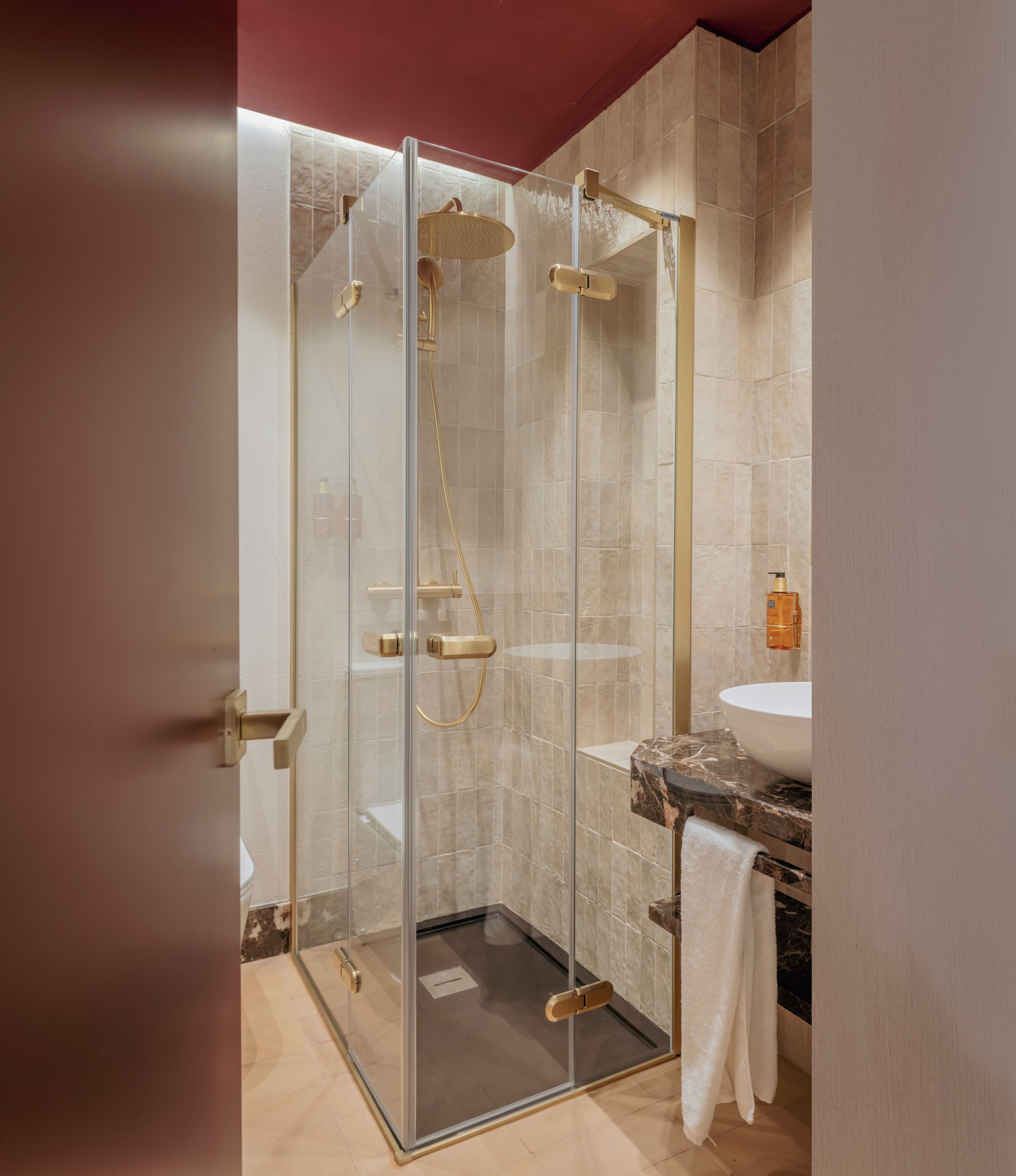 Un baño moderno con ducha cubierta por vidrio, lavamanos de mármol y una toalla colgada en la pared.