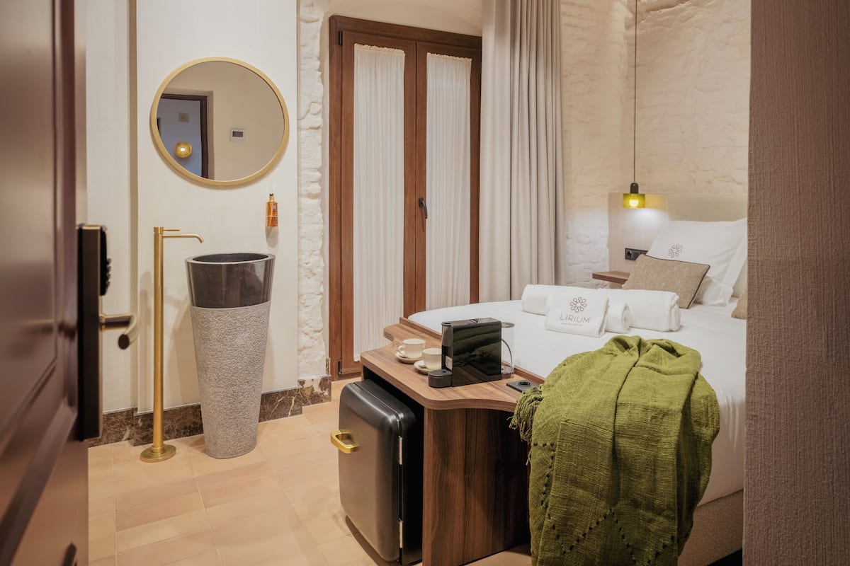 A hotel room with a bed, bedside table, lamp, and a trash bin.