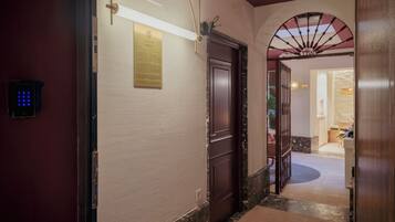 Um corredor com piso de mármore, porta de madeira escura e luminária na parede.