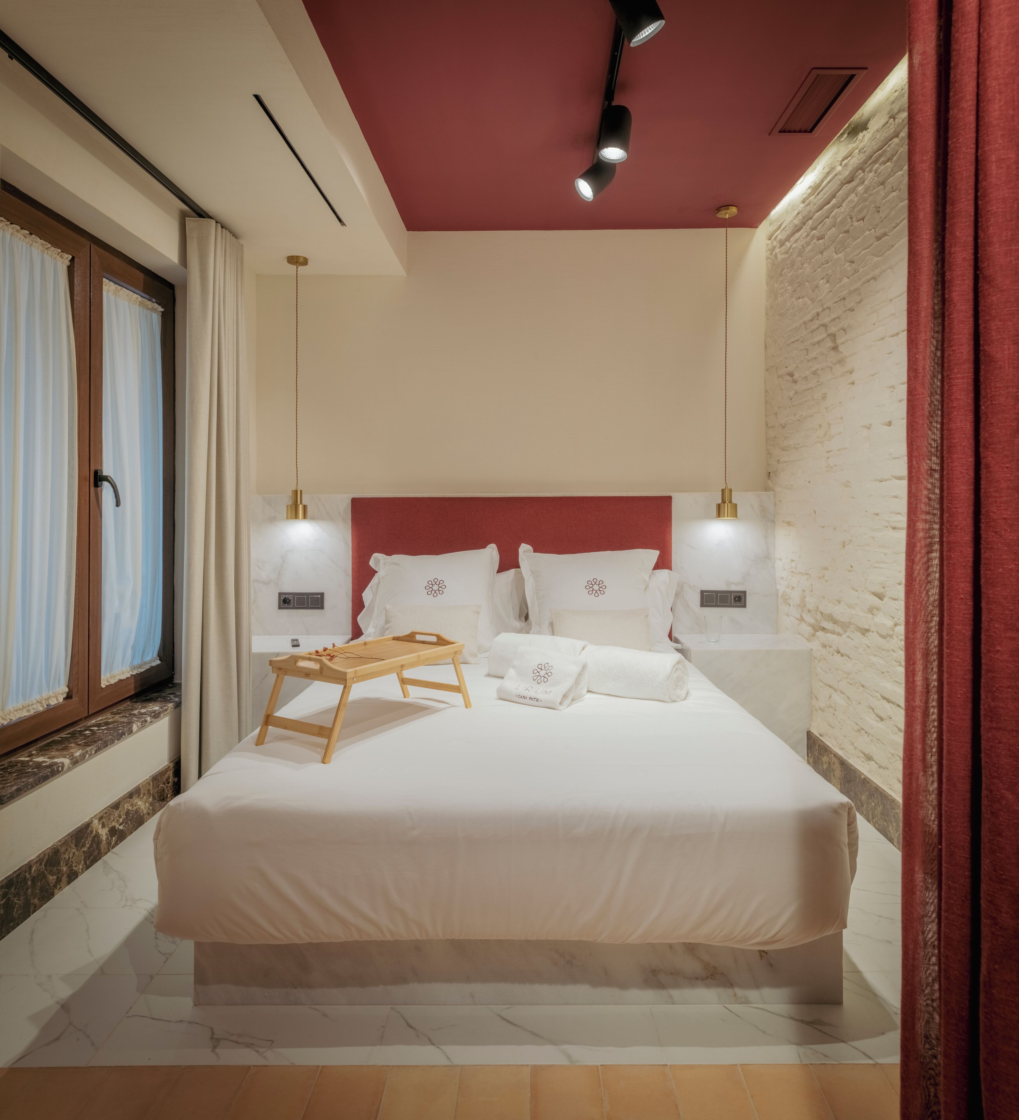 Habitación de hotel ordenada con una cama grande, mesitas de noche, una bandeja de madera y un techo rojo.