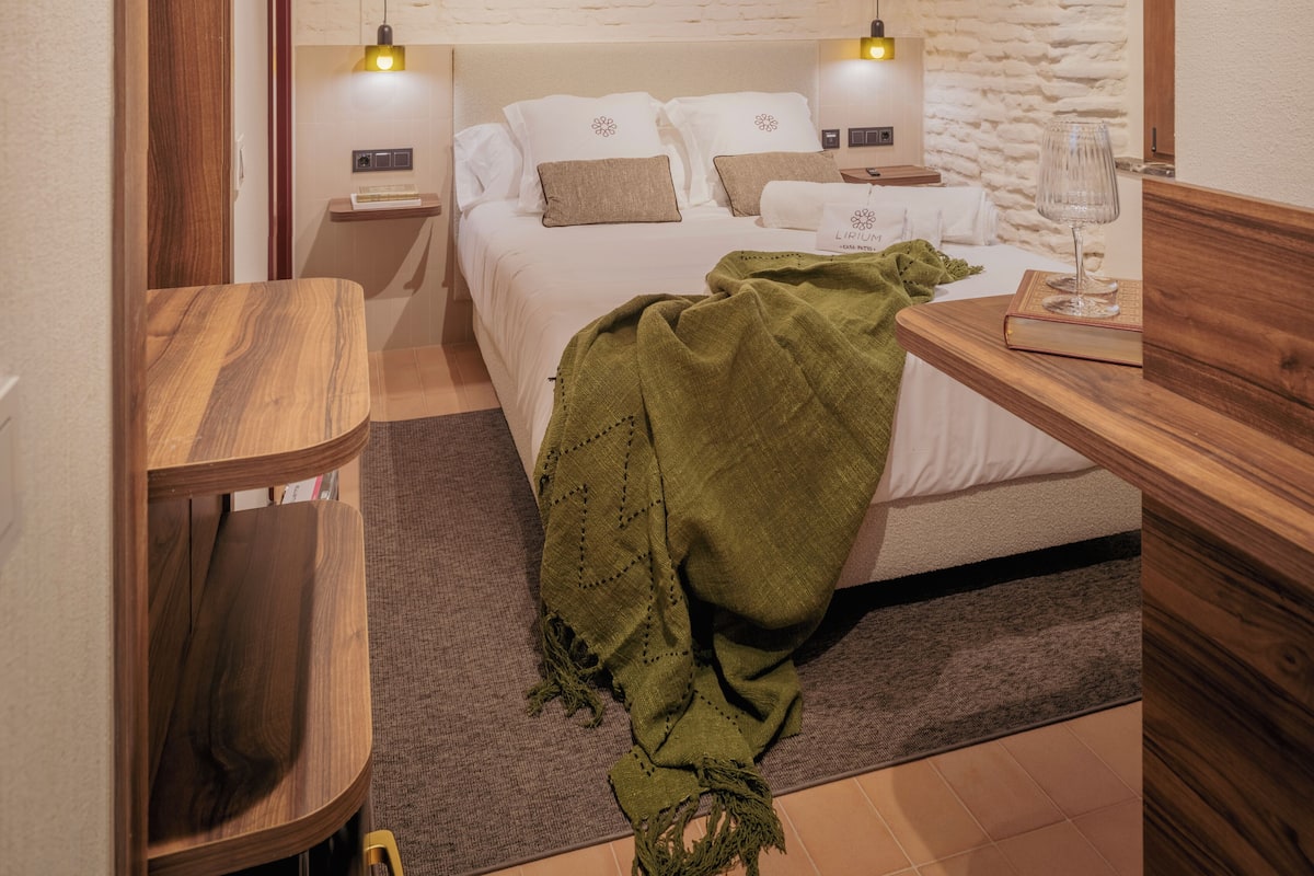 A compact bedroom with a bed, bedside tables, a wooden bench, and a brick wall.