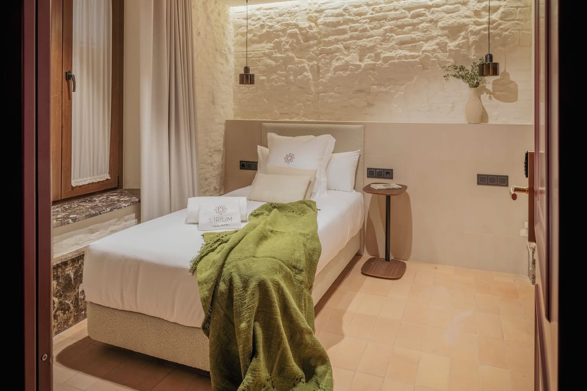 A modern bedroom with a bed, bedside tables, a green throw blanket, and a stone wall.
