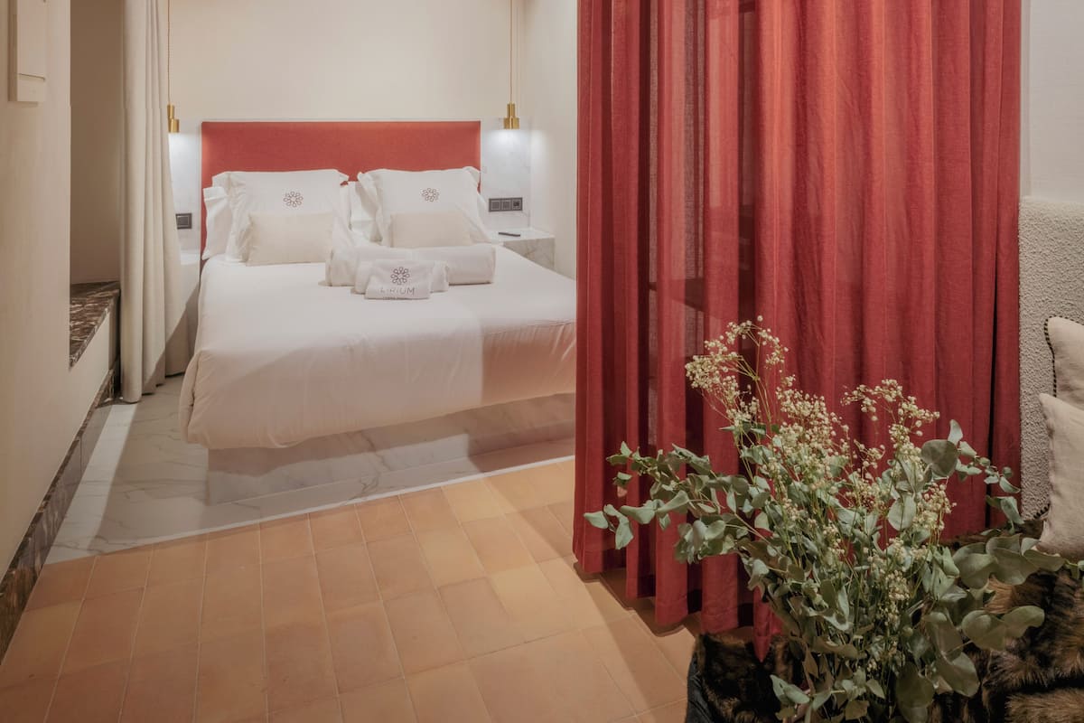 A modern bedroom with a large bed, a red curtain, and a plant.