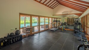 Une salle de sport équipée de matériel d’exercice, dotée de grandes fenêtres et offrant une vue sur une piscine.