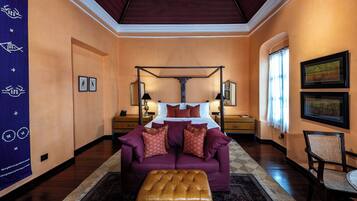 Un dormitorio con cama con dosel, un sofá morado y un otoman marrón.
