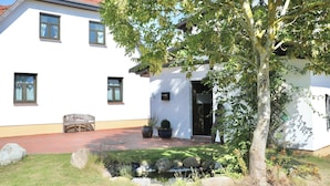 A two-story white building with a red-tiled roof, a small garden with a bench, and a tree in front. - Fewo Hiddensee Mecklenburg Pool Alte Schule Barlin (Dargun)