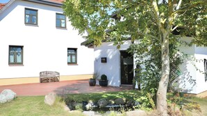 A two-story white building with a red-tiled roof, a small garden with a bench, and a tree in front. - Vacation apartment Rügen Alte Schule Barlin Mecklenburg Pool (Dargun)