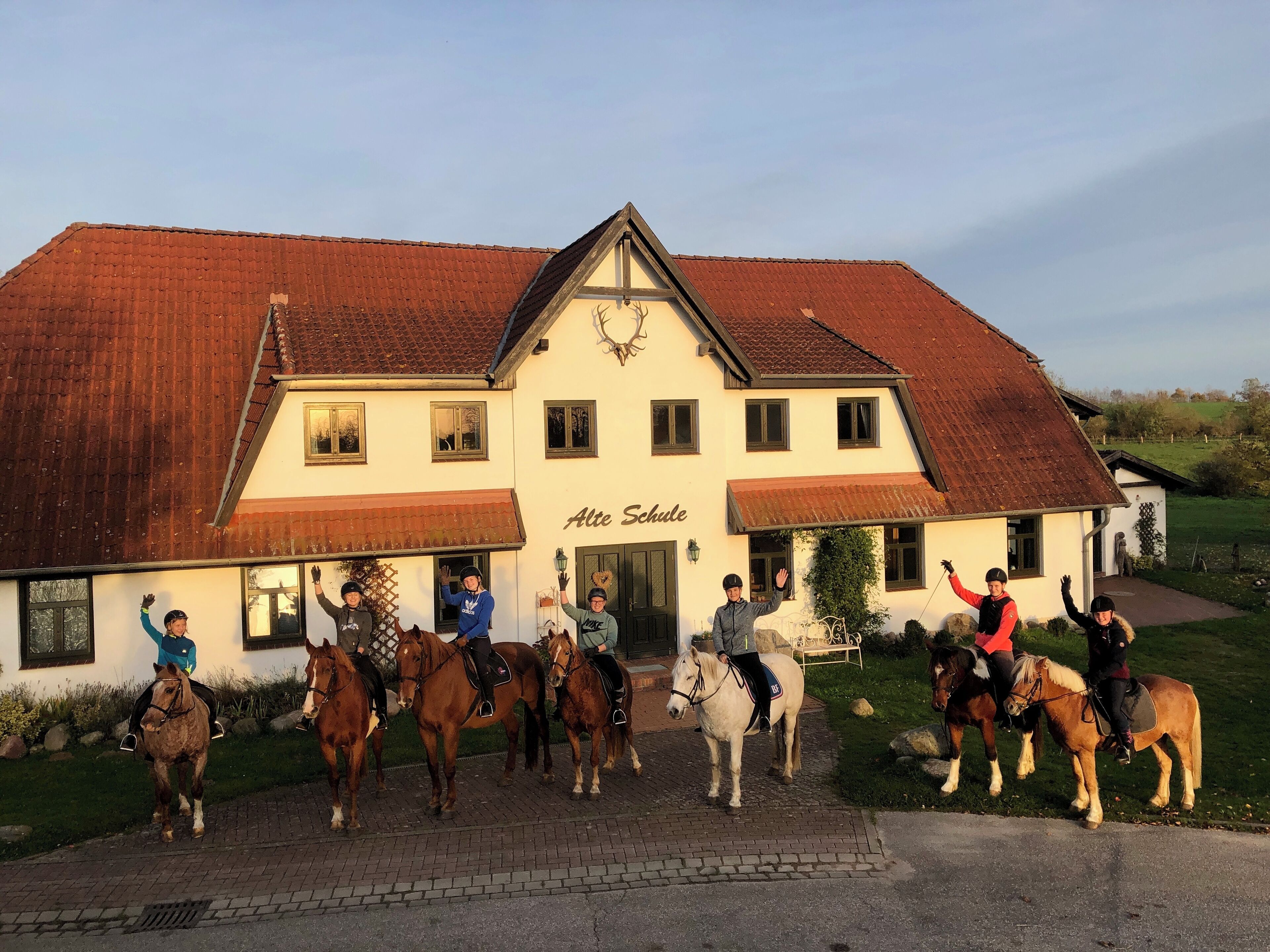 Un bâtiment sur lequel on peut lire l’inscription « Alte Schule », et un groupe de personnes à cheval devant.
