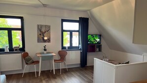 A cozy room with a wooden floor, a small table with chairs, a radiator, and a TV on a shelf.