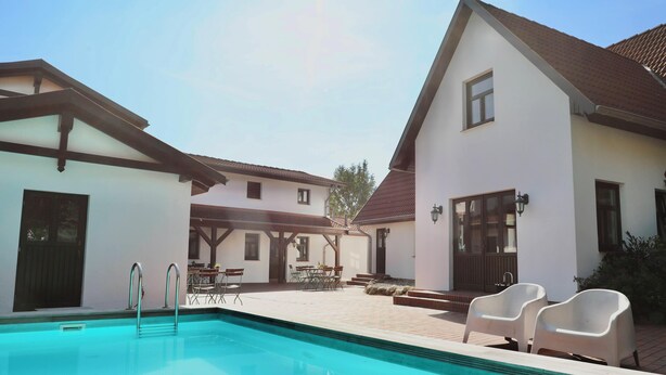 A swimming pool with a metal ladder, surrounded by a patio area with outdoor furniture and a covered seating area.
