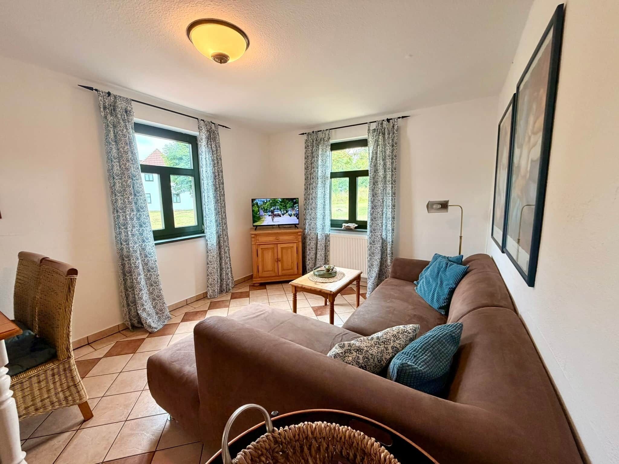 A living room with a sofa, a television, a wicker chair, a small table, and a window with curtains.