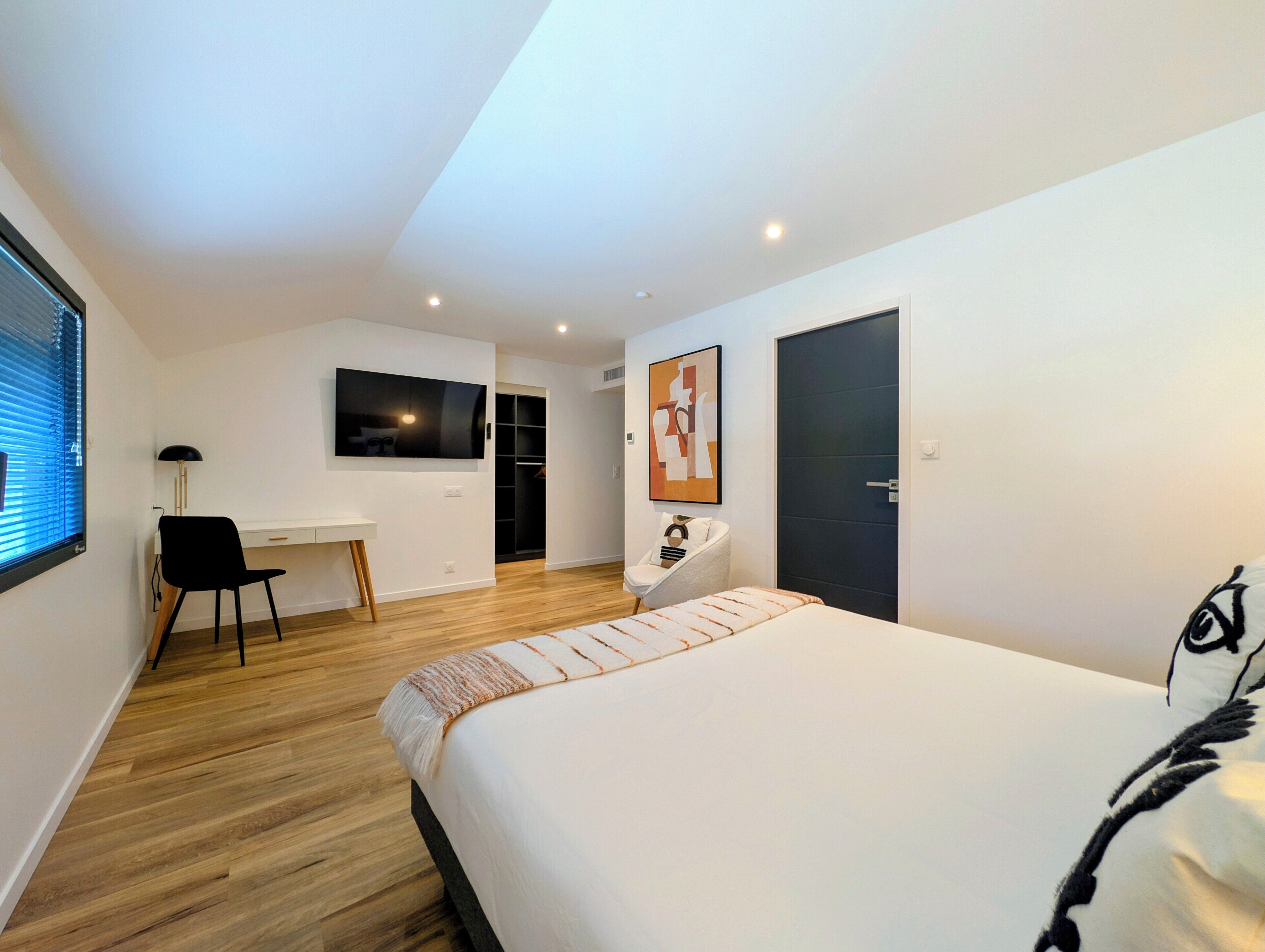 Un dormitorio con cama, escritorio, silla, armario y puerta.