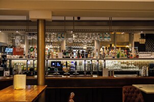 A bar area with a variety of bottles and glasses, a menu board, and a seating area with a wooden table and chairs.