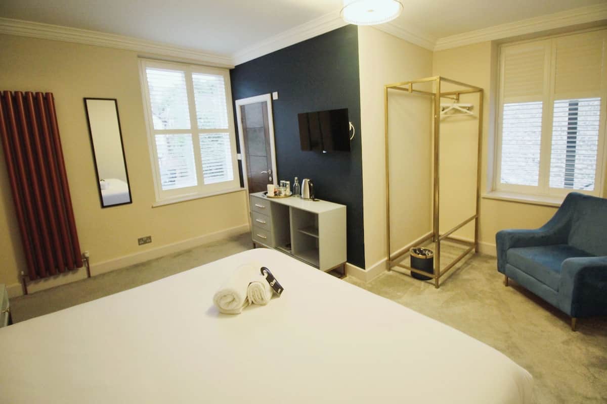 Une chambre d’hôtel avec un grand lit, un dressing, un coin salon et une fenêtre avec des stores.