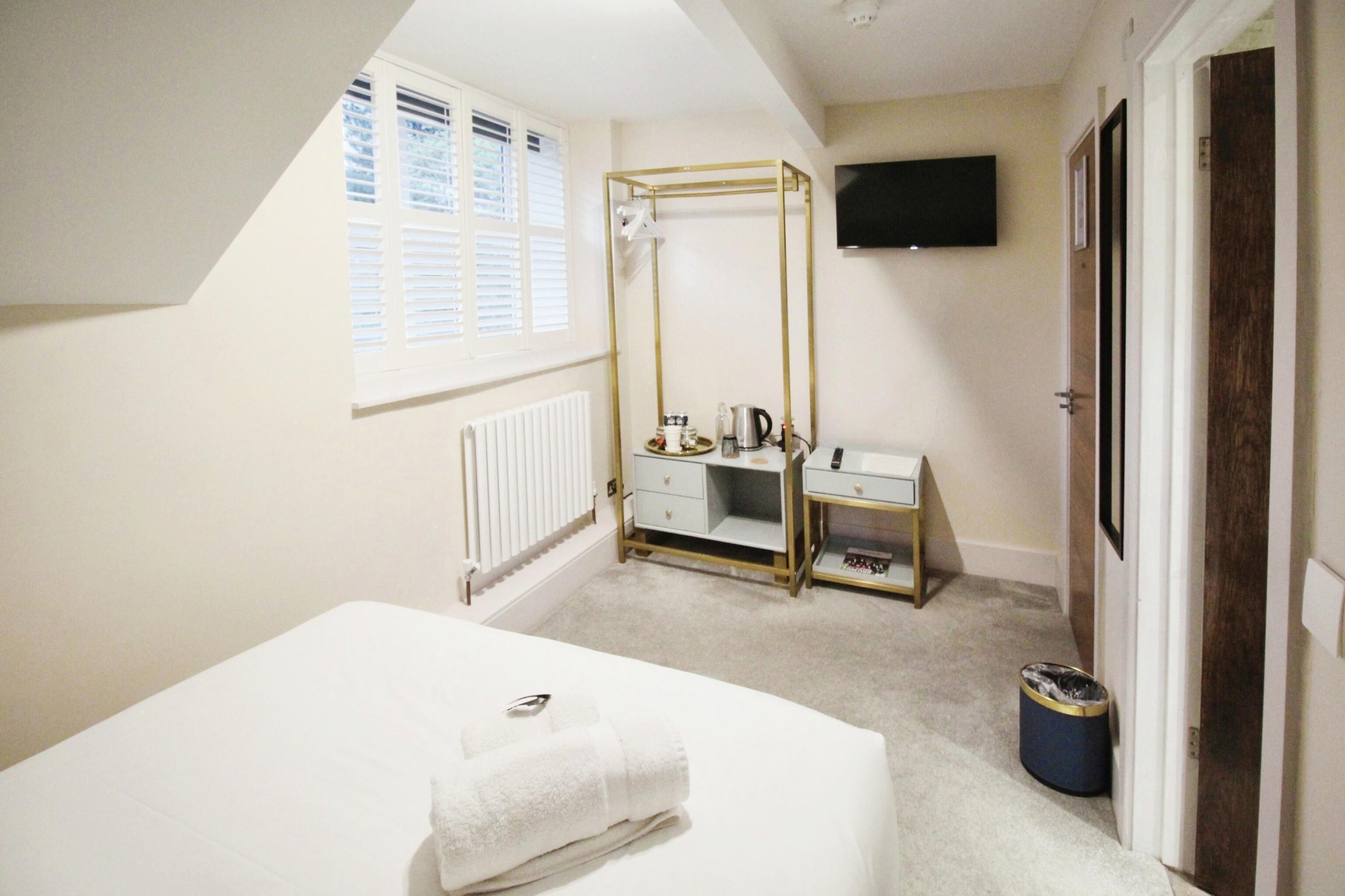 A bedroom with a bed, a vanity with a mirror, a radiator, a window with blinds, a television on the wall, and a door.