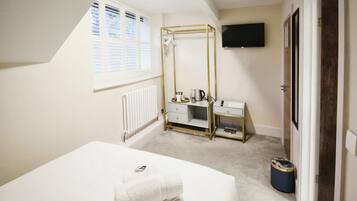 A bedroom with a bed, a vanity with a mirror, a radiator, a window with blinds, a television on the wall, and a door.