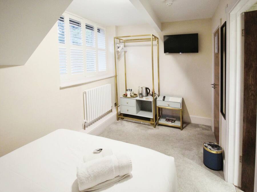 A bedroom with a bed, a vanity with a mirror, a radiator, a window with blinds, a television on the wall, and a door.