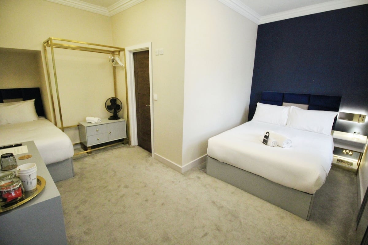 Une chambre d’hôtel comprenant un grand lit, une table de chevet, une commode, un bureau avec une chaise, une petite table avec un plateau, et un dressing.