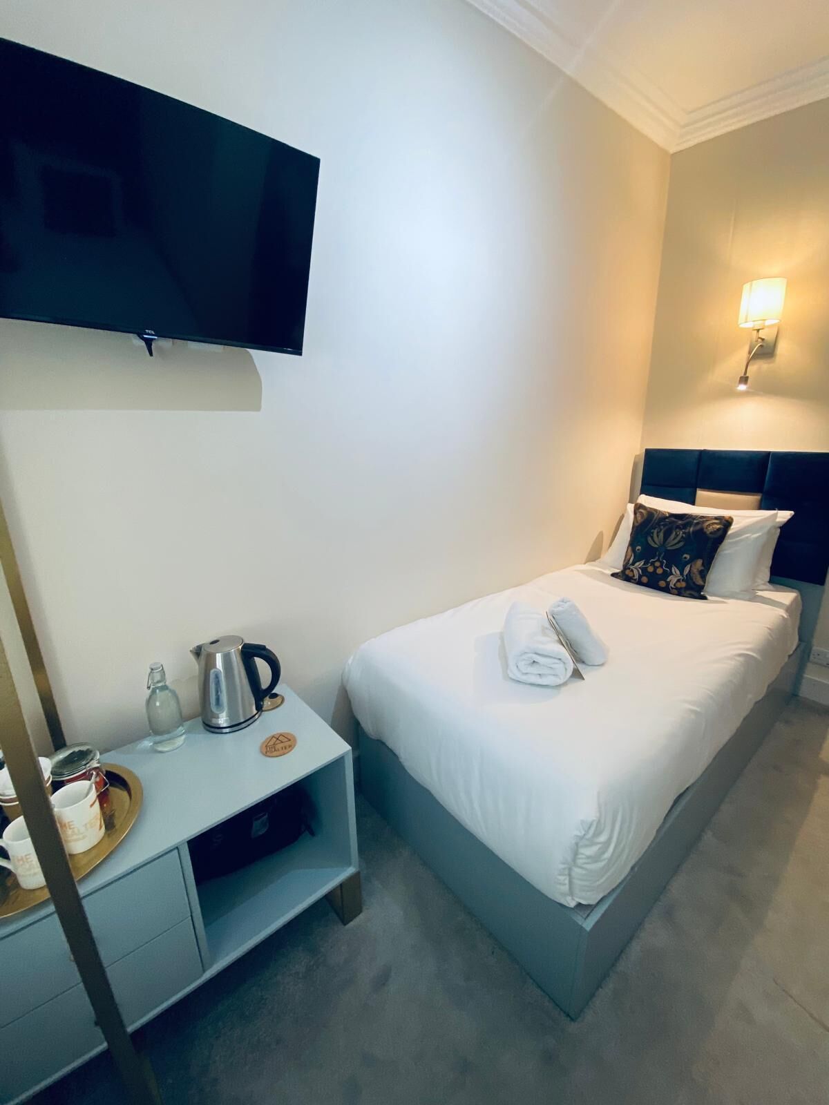 A hotel room with a bed, a nightstand, a television, and a wall-mounted light.
