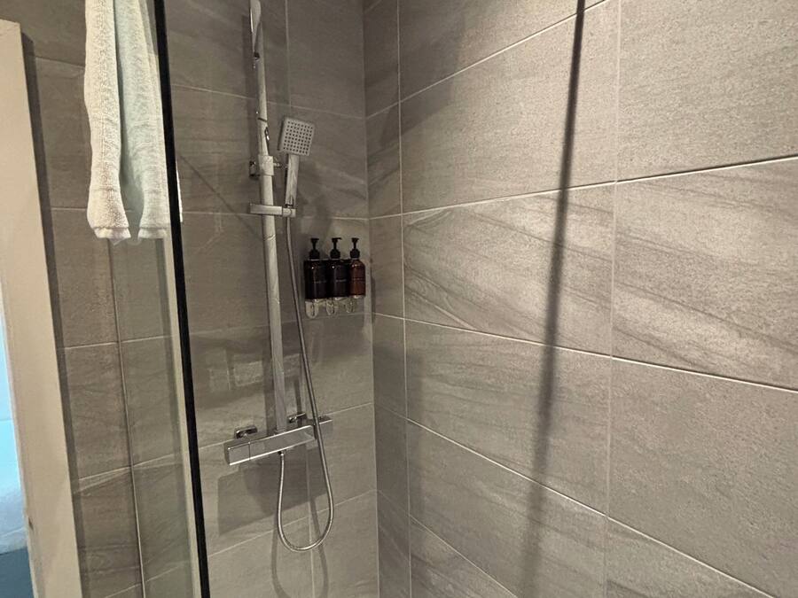 Et moderne badeværelse med en glasvæg omkring bruseren, et hvidt badekar og grå flisegulve.