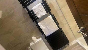 Un baño con un toallero negro que sostiene dos toallas blancas, un inodoro blanco y una cabina de ducha con paredes de vidrio.
