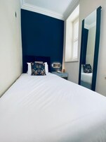 A hotel room with a large bed, a nightstand, a mirror, and a window with blinds.