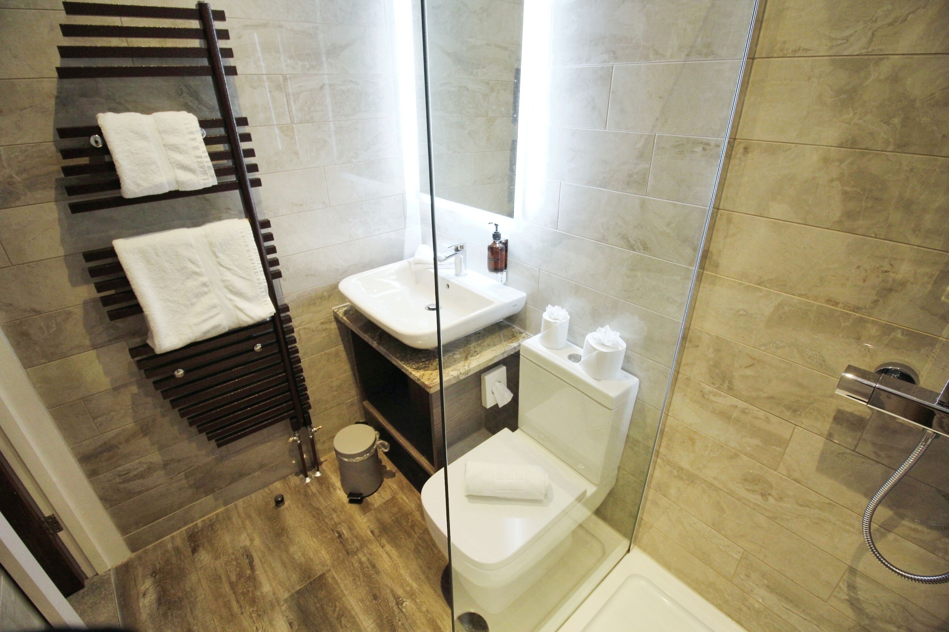 A modern bathroom with a glass shower enclosure, a built-in sink, and a towel rack with three towels.