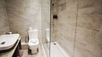 A modern bathroom with a glass-enclosed shower, a white sink, and a toilet.