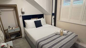 Un dormitorio con cama, mesita de noche, lámpara y ventana con persianas.