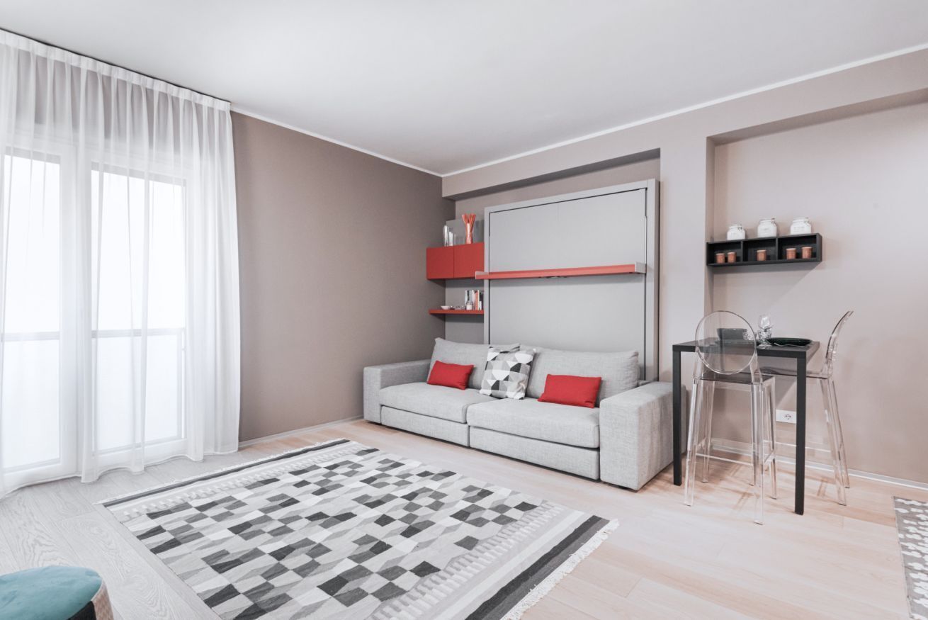 Ein modernes Wohnzimmer mit grauem Sofa, roten Kissen, einem schwarzen Couchtisch und einem gemusterten Teppich.